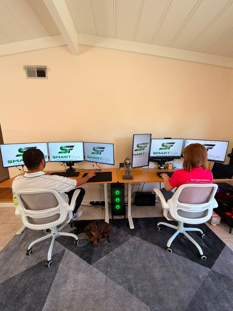 Man and woman at a desk with multiple monitors showing SMARTFIX logos and a dog.