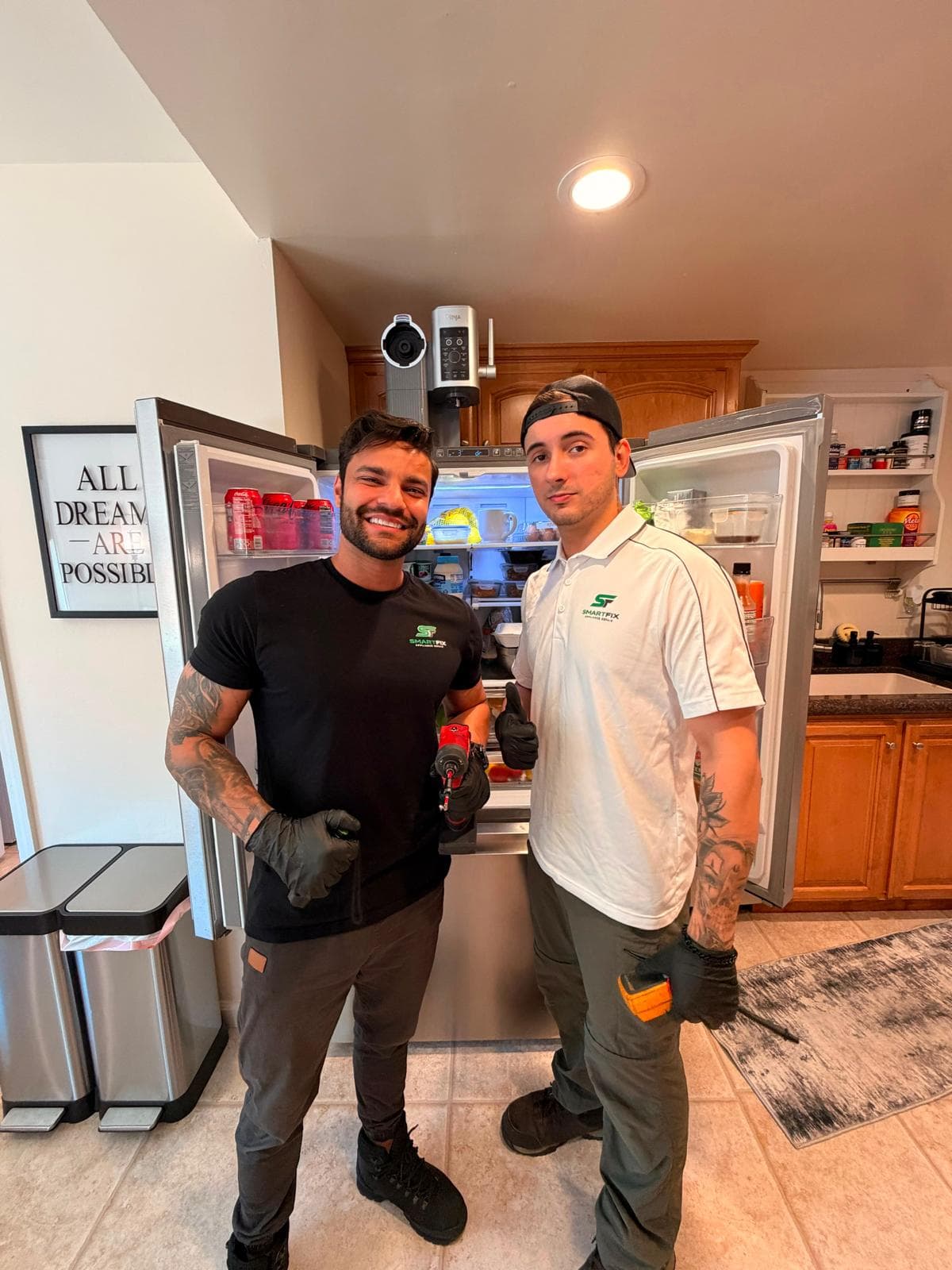 Two SmartFix appliance repair technicians posing with tools in front of an open kitchen refrigerator.